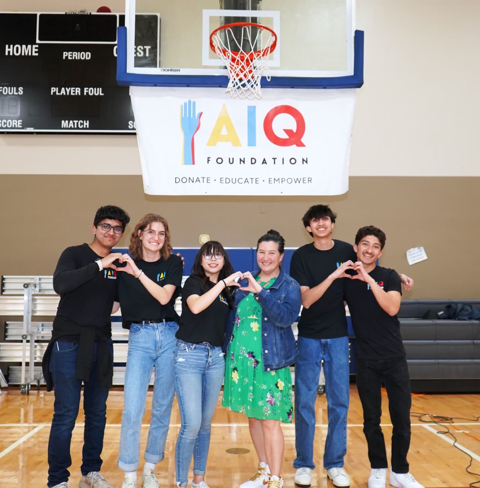 AIQ volunteers making heart signs under the AIQ banner at a charity basketball event